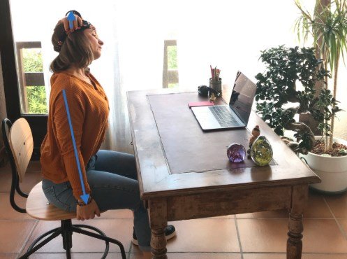 Photo d'une femme assise à son bureau qui étire ses trapèzes en tenant son fauteuil avec une main et étire sa tête dans le sens opposé avec l'autre main